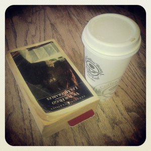 A battered paperback copy of Les Misérables with a bookmark visible about halfway through, next to a cardboard cup of coffee