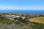 A park seen from above: Grassy fields, some trees, a long, low, flat building, and basketball courts are visible. A few lines of houses can be seen past the park, but then the land gives way to ocean. On the horizon you can see the two lobes of Catalina Island in silhouette.