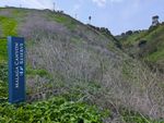 Hillside covered with brush and low greenery. A vertical blue sign identifies Malaga Canyon Reserve.