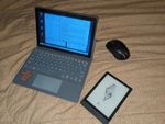 PineTab2 in keyboard case, with a mouse and a Boox Poke3 eReader for scale. A tablet computer, about the size of two eBook readers placed next to each other, in a thin plastic case with an attached keyboard and trackpad. The keyboard looks a bit cramped, but not too horrible. The tablet is displaying a Linux desktop environment with icons along the left, a taskbar along the bottom, and three windows open: a text editor with a document written in markdown, a web browser showing a rendered page, and a file manager showing a few icons of markdown files.