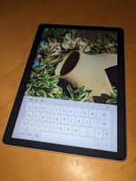 The same tablet, this time placed vertically and without the attached keyboard. It's showing the same garden photo, cropped to the middle, and an on screen keyboard takes up a bit less than th elower third of the display.