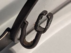 Close-up of glasses frames with a metal clip attached, shaped like an elongated, rectangular letter C with two bumps visible on the inside.